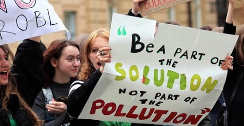 Greta Thunberg in manifestazione, una ragazza a destra tiene un cartello con uno slogan